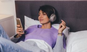 Happy woman at home on comfy bed wearing warm clothes pullover, listen music